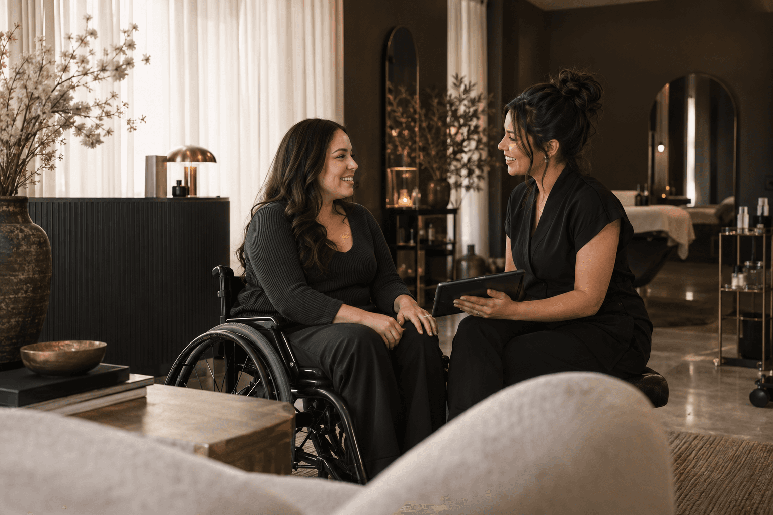 A client using a wheelchair talking with a lash artist at a step-free studio reception
